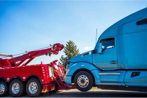 Heavy duty tow truck helping a large blue semi truck